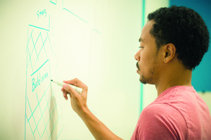 Tony Kershaw, the student entrepreneurial consultant and program coordinator for IDEA, sketches a floor plan on a whiteboard in preparation for the Rube Goldberg machine. The IDEA project will be built in Marshall Square Mall on Oct. 25 by student groups.