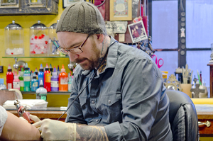 David Rose tattoos a client at Halo Tattoo on Marshall Street. He opened the tattoo parlor in 1997. Rose helps clients design their tattoos and enjoys the artistic process. 