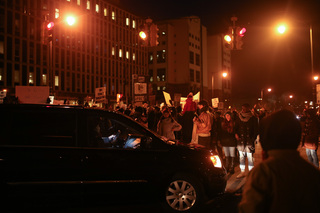 A car attempts to drive by the marchers at the intersection in front of the Patrick J. Corbett Justice Center.